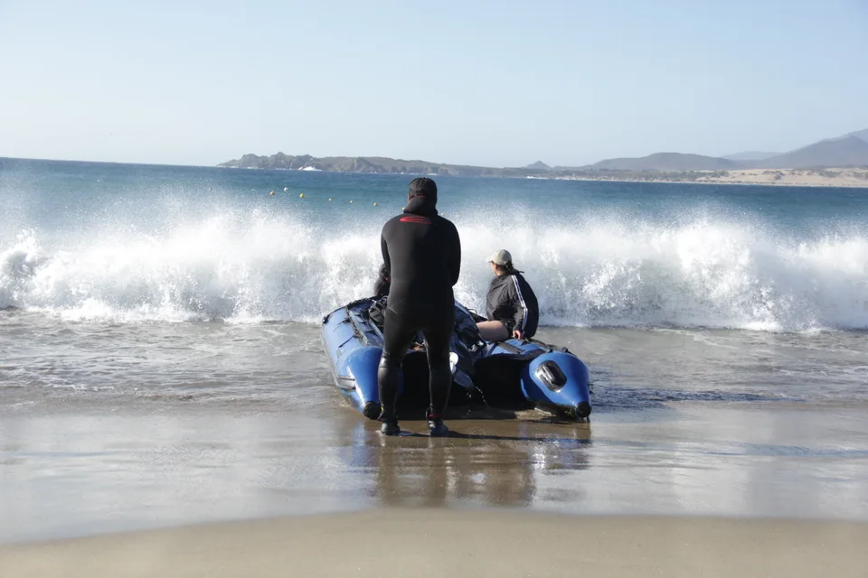 Tripulantes en bote azul sobre una ola